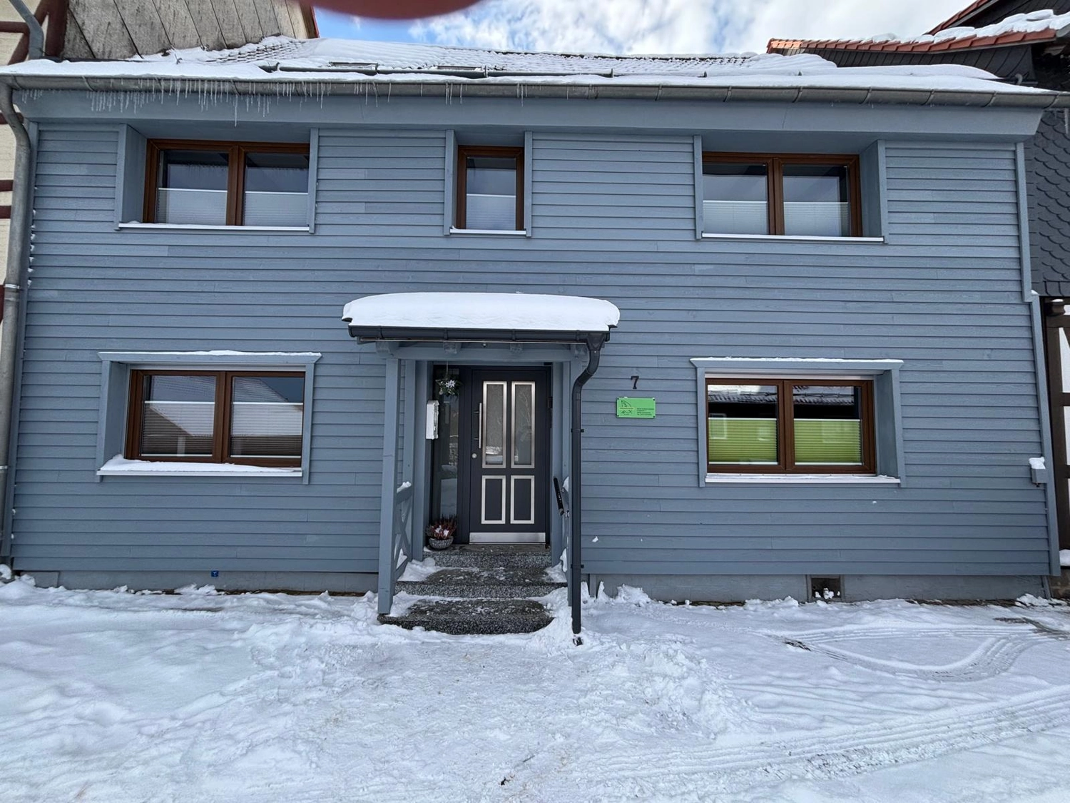 Ecklebe - Ferienwohnung - Ein zweistöckiges, hellblaues Haus mit grauem Dach und mehreren Fenstern, bedeckt mit Schnee.