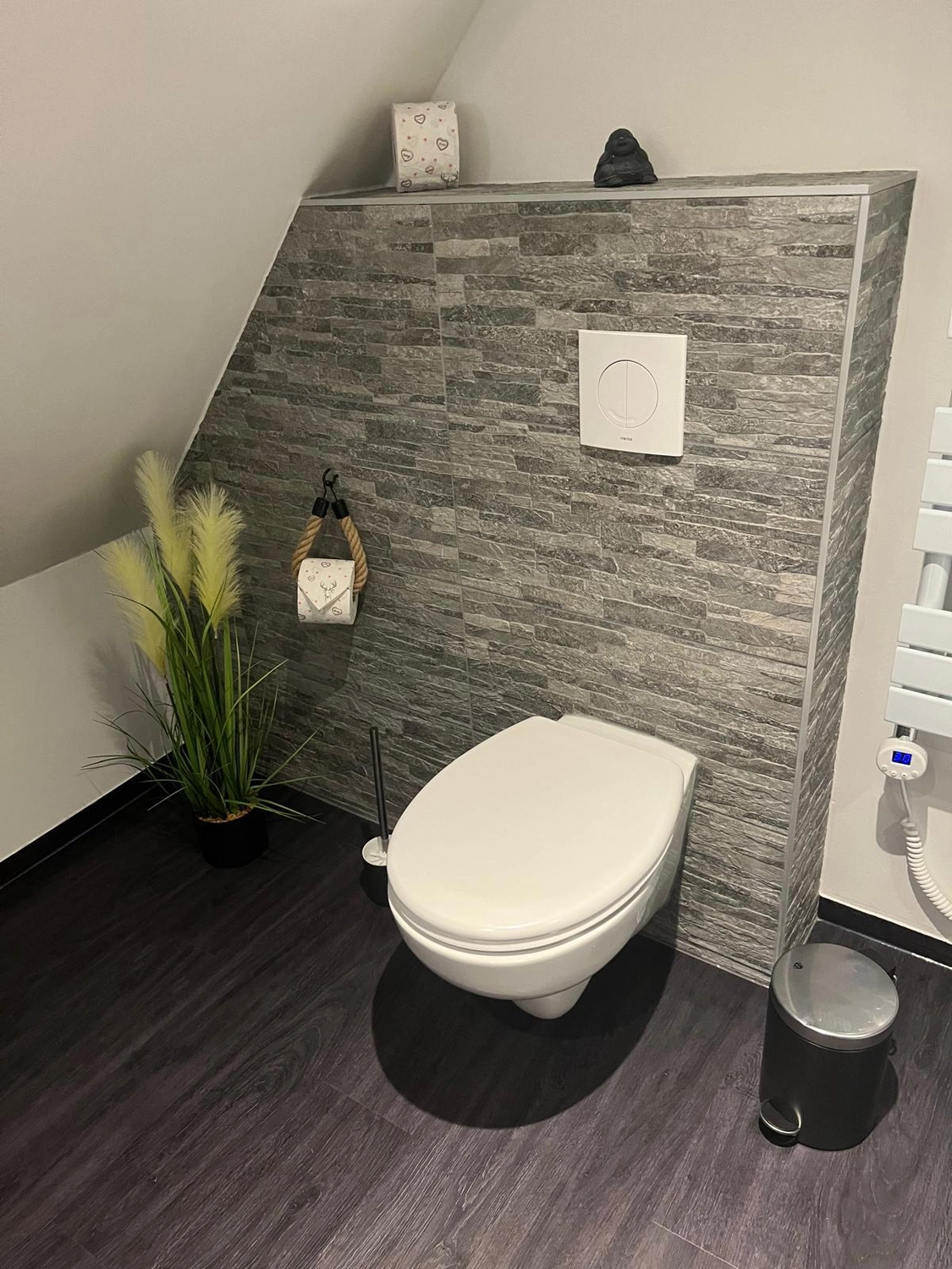 Ecklebe - Ferienwohnung - Eine Badezimmerecke mit Toilette, einer Akzentwand mit Steinmuster und einer Pflanze.