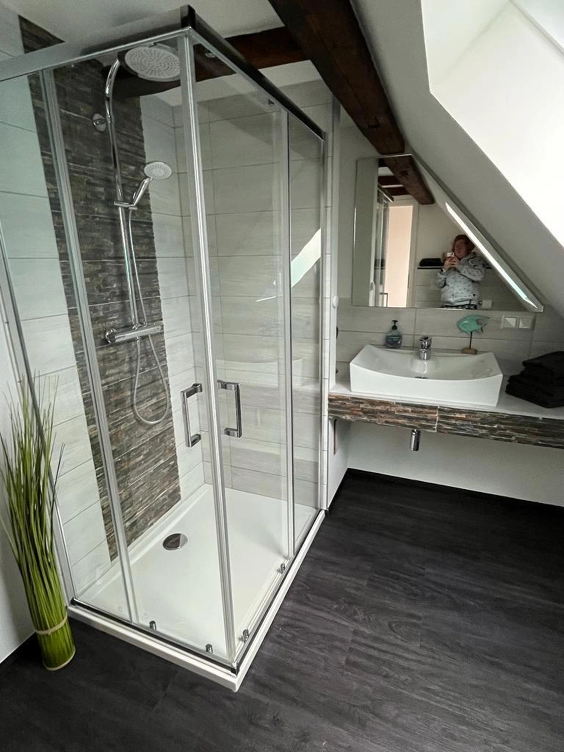 Ecklebe - Ferienwohnung - Ein modernes Badezimmer mit Duschkabine aus Glas, Waschbecken mit Holzunterschrank und dunklem Bodenbelag.