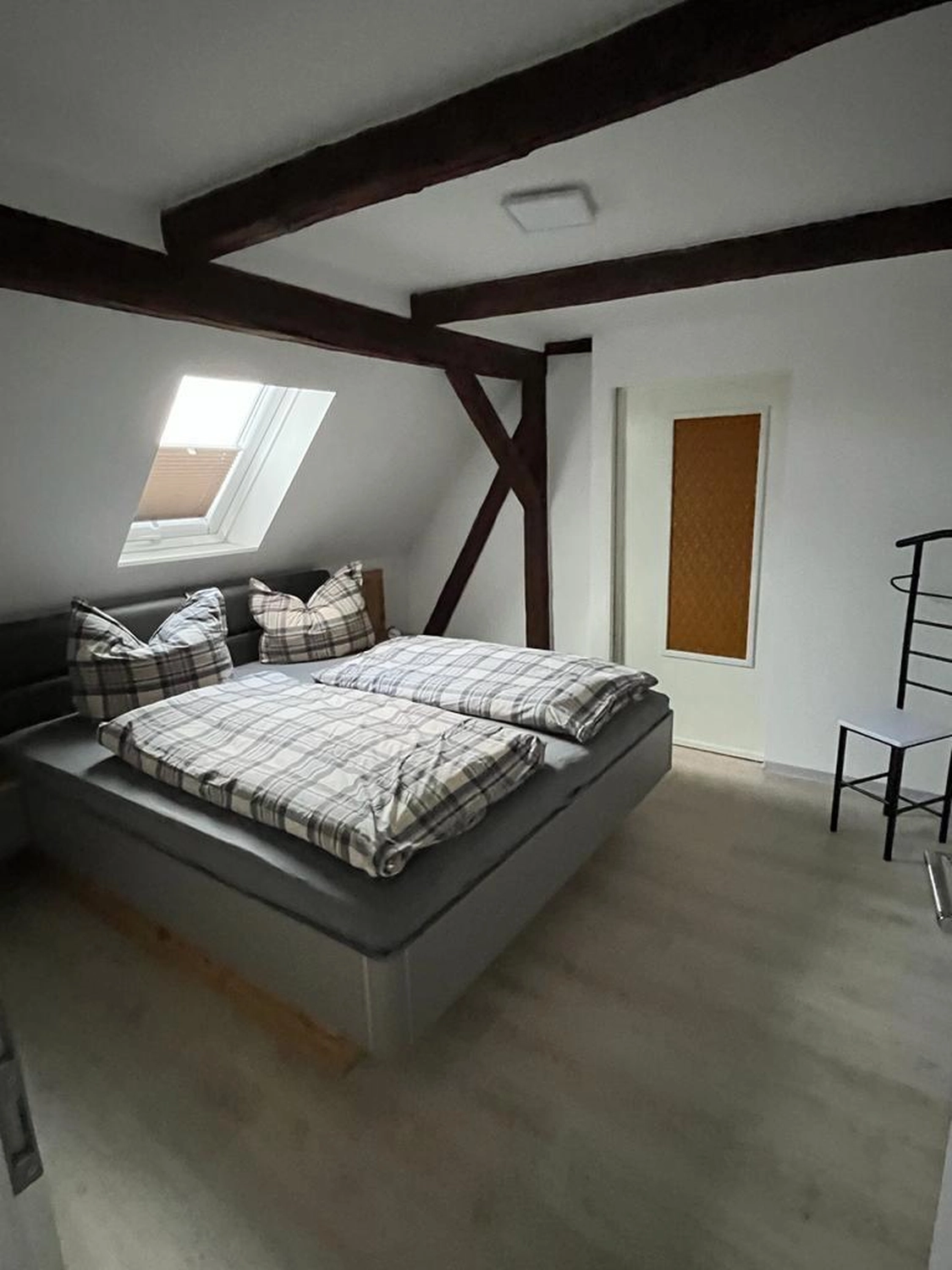 Ecklebe - Ferienwohnung - Ein Dachgeschoss-Schlafzimmer mit Doppelbett, freiliegenden Holzbalken, einem kleinen Sofa und einem Dachfenster.