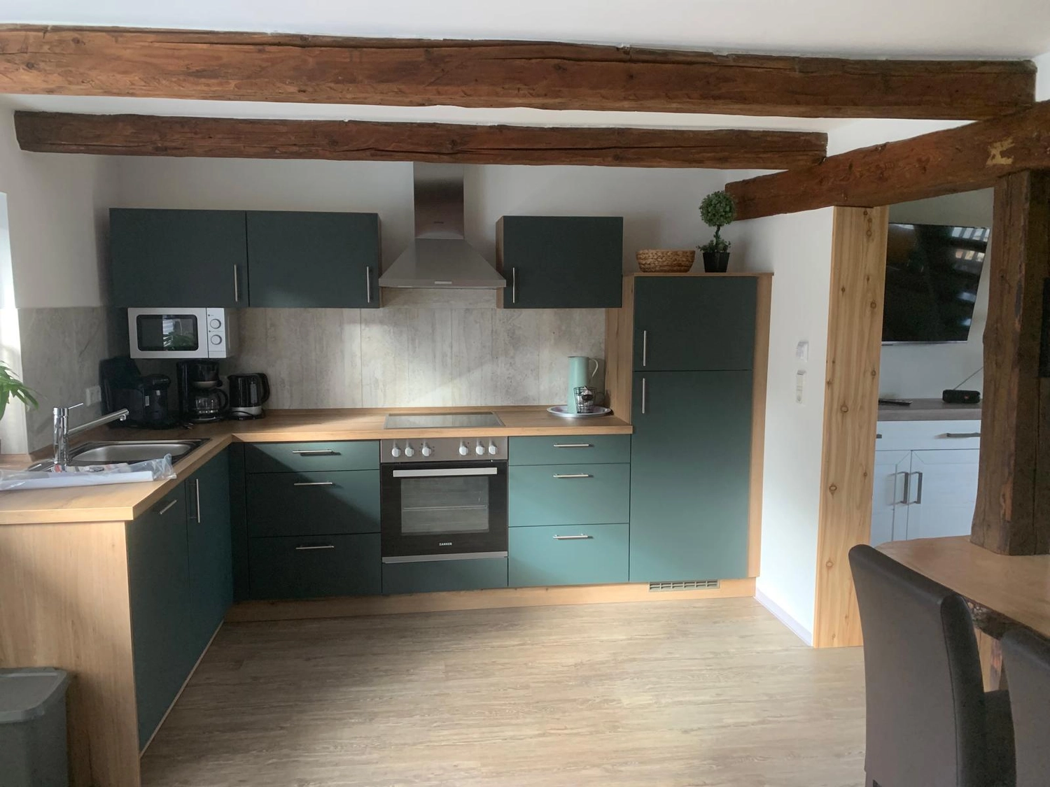 Ecklebe - Ferienwohnung - Eine moderne Küche mit dunkelgrünen Schränken, Holzbalken an der Decke und Edelstahlgeräten.