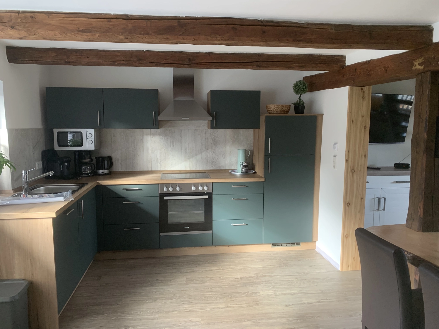 Ecklebe - Ferienwohnung - Eine moderne Küche mit dunkelgrünen Schränken, Holzbalken an der Decke und Edelstahlgeräten.