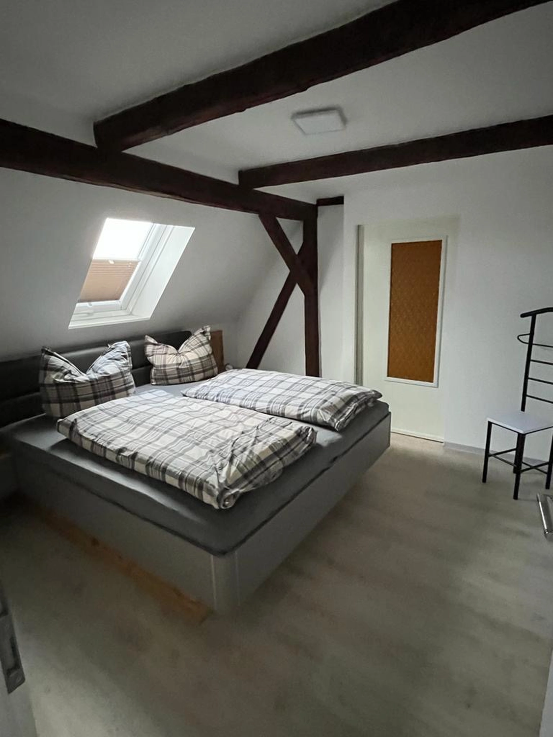 Ecklebe - Ferienwohnung - Ein Dachgeschoss-Schlafzimmer mit Doppelbett, freiliegenden Holzbalken, einem kleinen Sofa und einem Dachfenster.