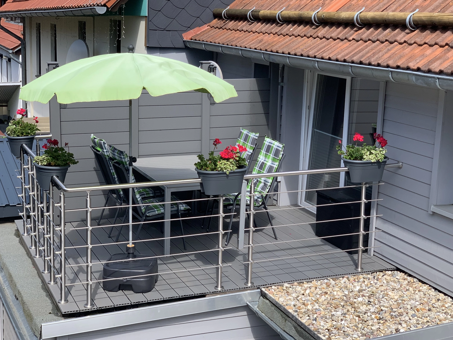 Ecklebe - Ferienwohnung - Ein Balkon oder eine  Terrasse im Freien mit einem grünen Sonnenschirm, Topfpflanzen, einem Metallgeländer und einem gefliesten Boden.