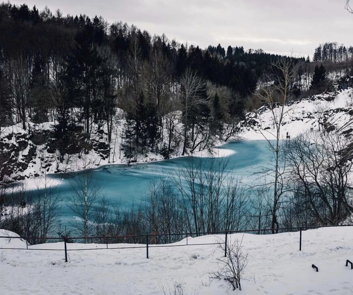 Ecklebe - Ferienwohnung - Ein teilweise zugefrorener, leuchtend türkisfarbener See, umgeben von schneebedeckten Ufern und einem dichten Wald aus immergrünen und kahlen Bäumen im Winter.