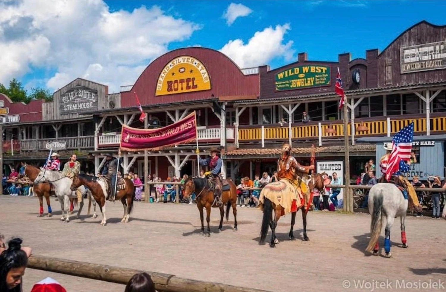 Ecklebe - Ferienwohnung - Außenansicht eines Gebäudes mit einem Schild mit der Aufschrift „KYTOW HOTEL WILD WEST“, im Vordergrund ein hölzerner Steg, eine rote Kanu-Dekoration und Reiter.