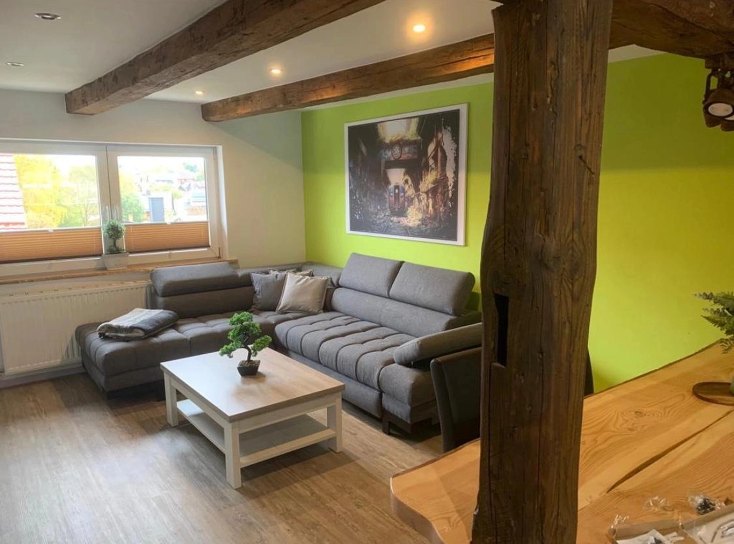 Ecklebe - Ferienwohnung - Ein Wohnzimmer mit grünen Akzentwänden, freiliegenden Holzbalken, einem grauen Sofa, einem Couchtisch und einem gerahmten Bild an der Wand.