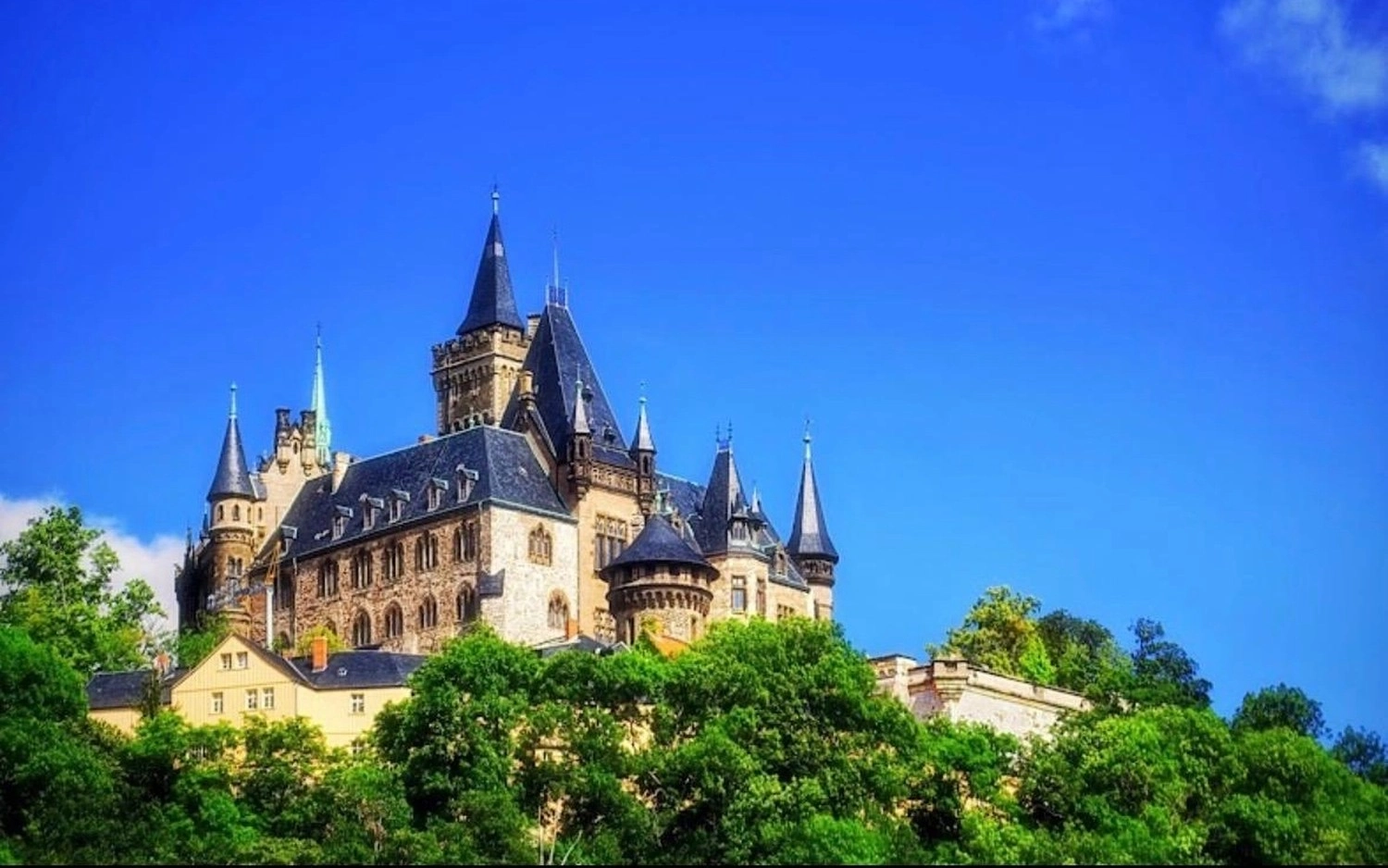 Ecklebe - Ferienwohnung - Ein großes, historisches Schloss auf einem grünen Hügel vor strahlend blauem Himmel.