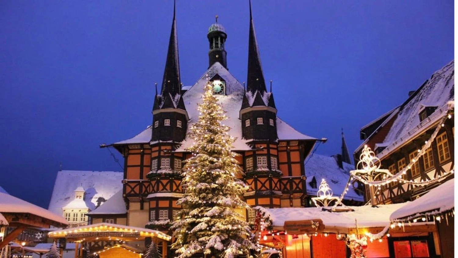 Ecklebe - Ferienwohnung - Verschneites mittelalterliches Fachwerk-Rathaus mit Türmen hinter einem beleuchteten Weihnachtsbaum in der Nacht.